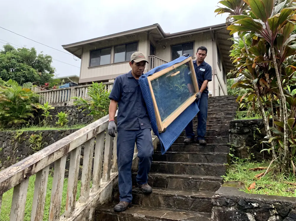 Dua pekerja mengangkut pintu kaca sauna lewat tangga